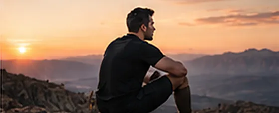 A man sitting on a ridge looking out at a desert sunset